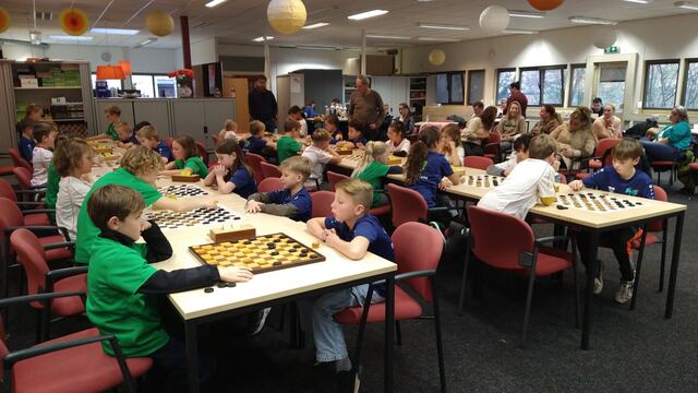 Volle zaal met kinderen achter damborden